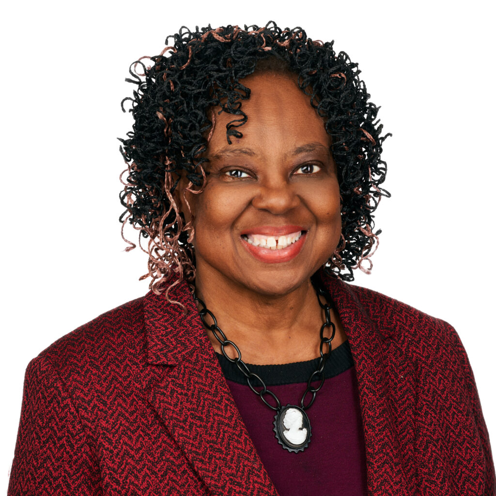 Smiling person with short hair, wearing red earrings, a red necklace, and a red blazer.